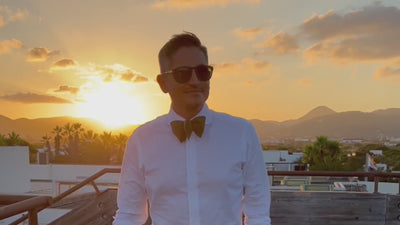 Man walking down the sunset wearing a white button up shirt and a solid colored silk bow tie